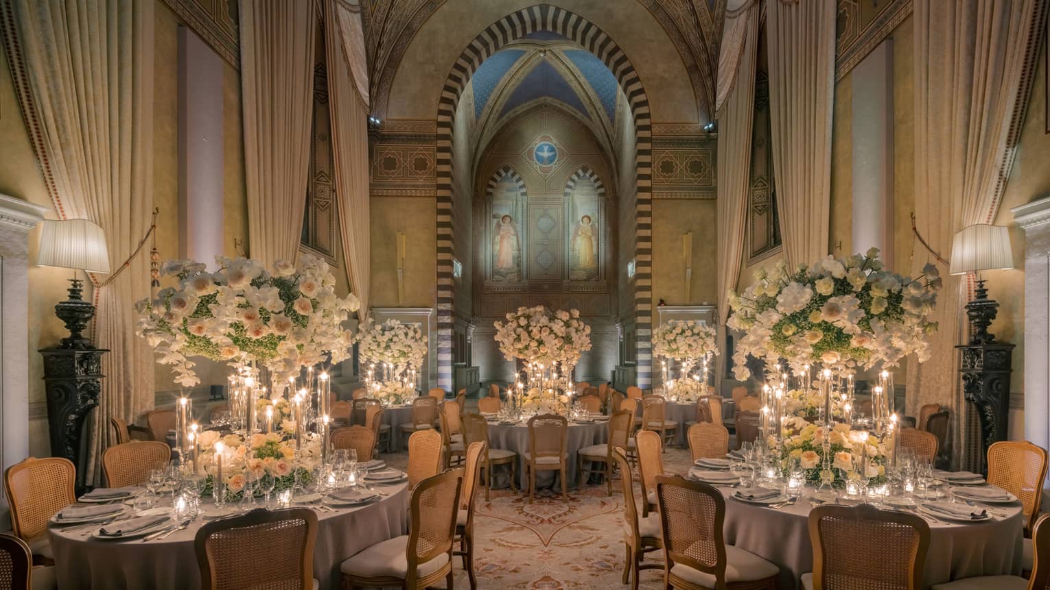 Grand dining room with tall arched ceilings and round elegantly set tables with tall white flower centrepieces