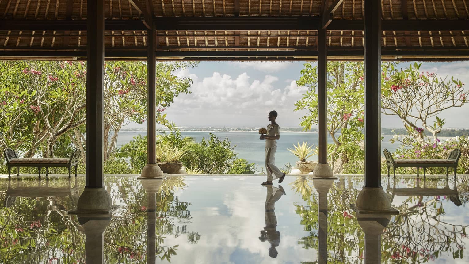 Hotel staff carrying flowers reflected onto floor of open-air pavilion 