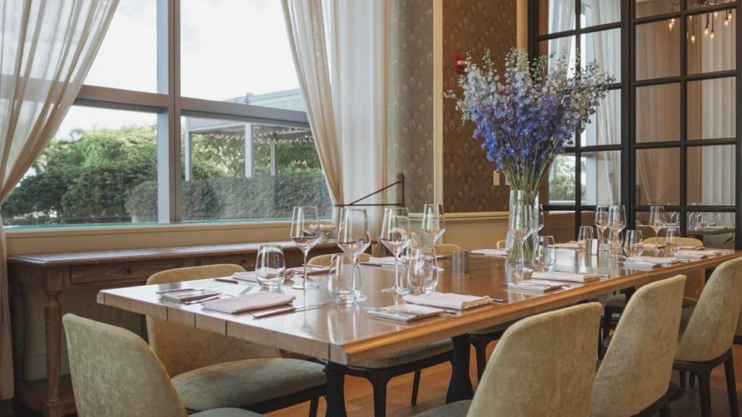 A large dining table with blue flowers near a large window.