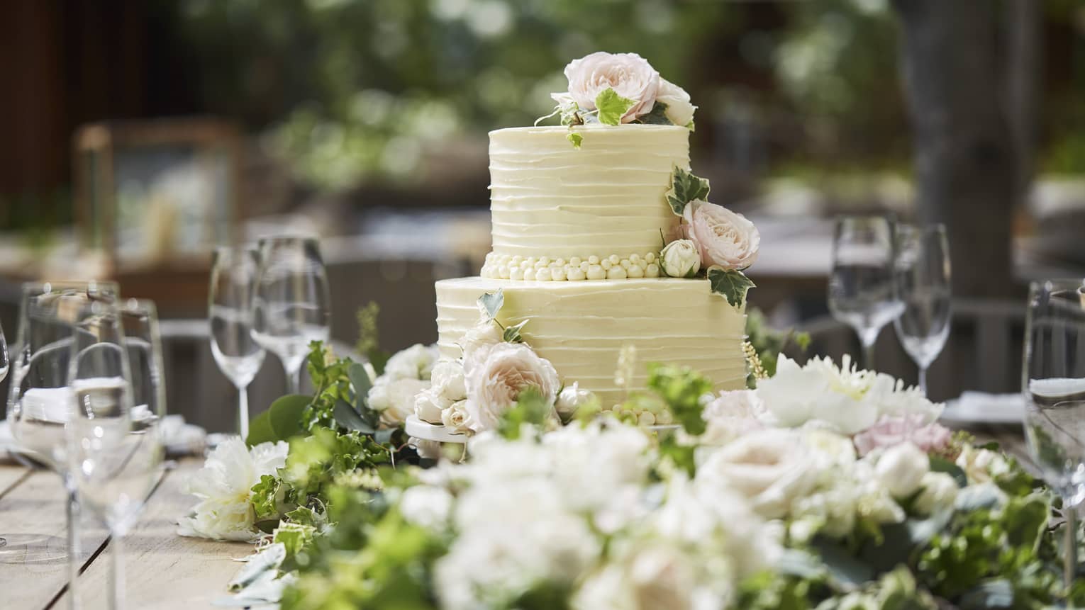 Two-tiered white wedding cake on banquet table with wine glasses, flowers