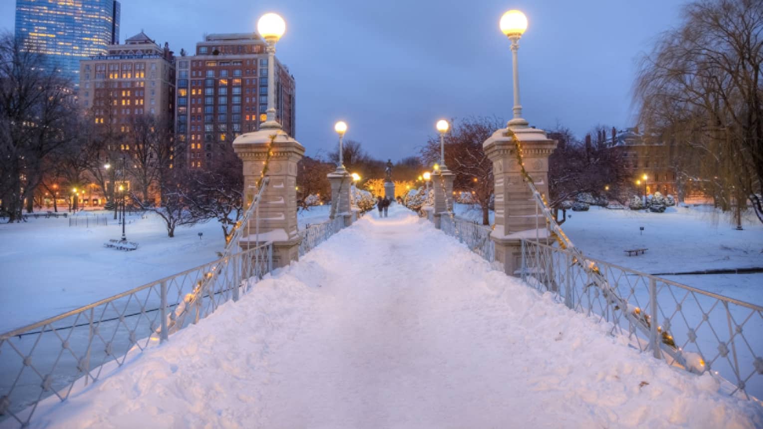 Bridge at night time covered in snow with city buildings in the background