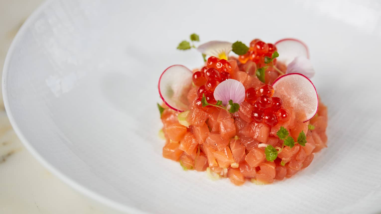 Raw salmon cut into small pieces with fish roe and herbs.