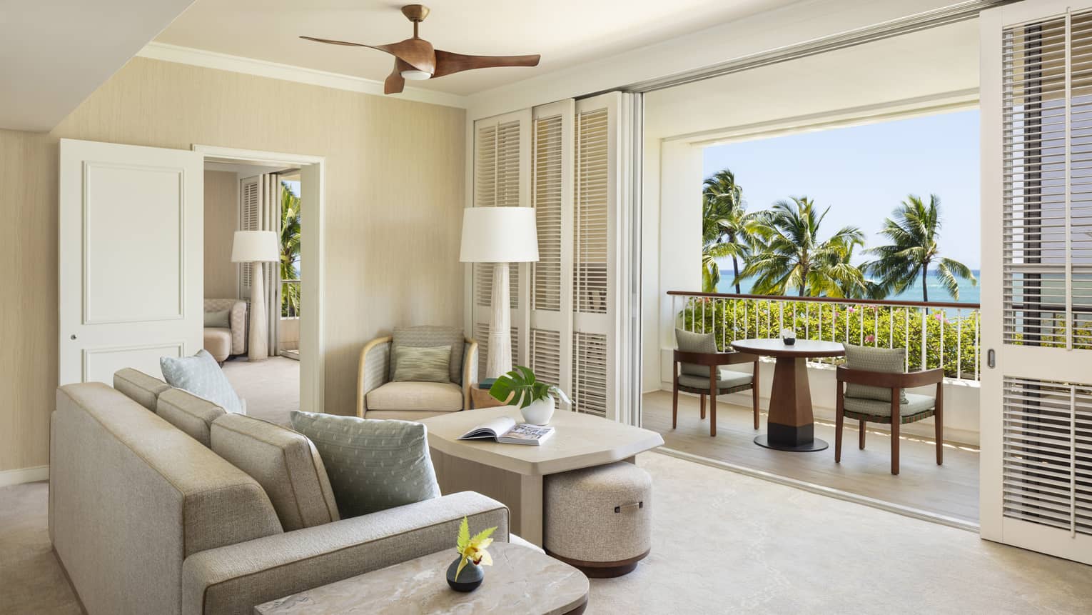 Elegant resort suite living room, featuring a beige sofa facing a furnished balcony with tropical ocean views