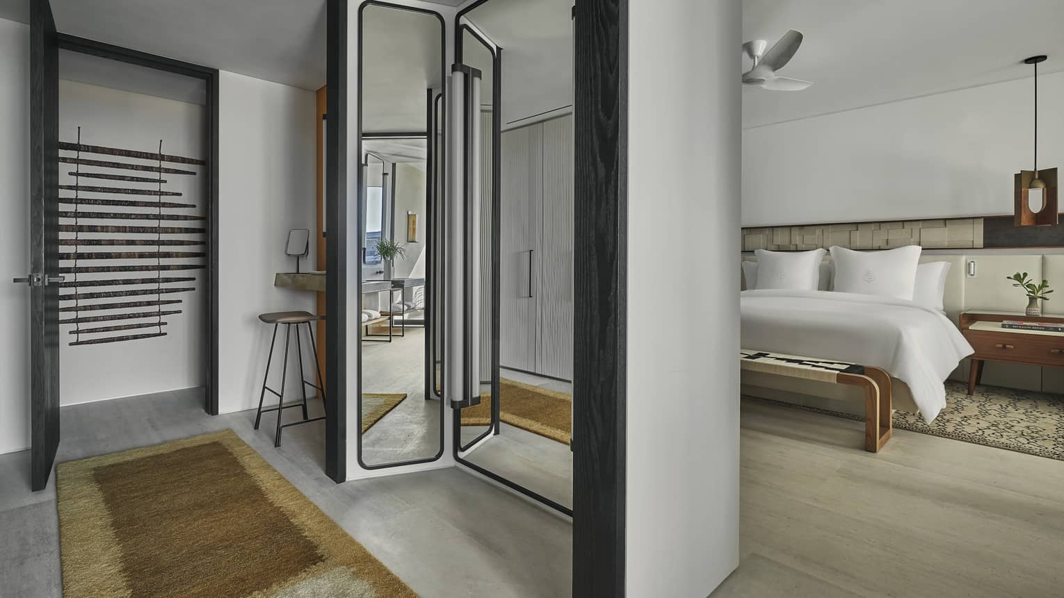 A hotel room with a bed, mirror, bench and small table.