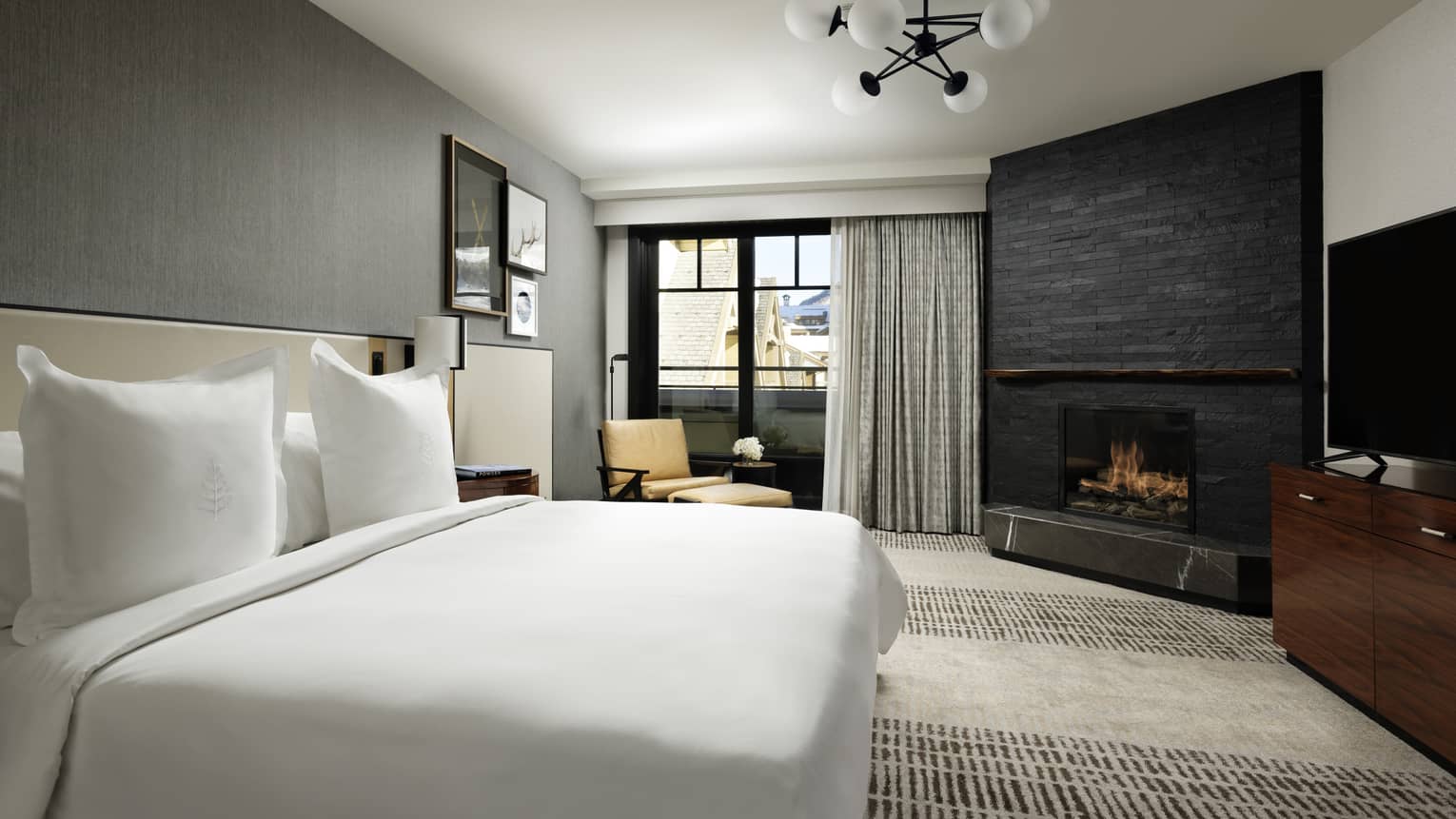 One-bedroom suite with King bed, corner fireplace, floor-to-ceiling window with grey curtains, yellow chaise