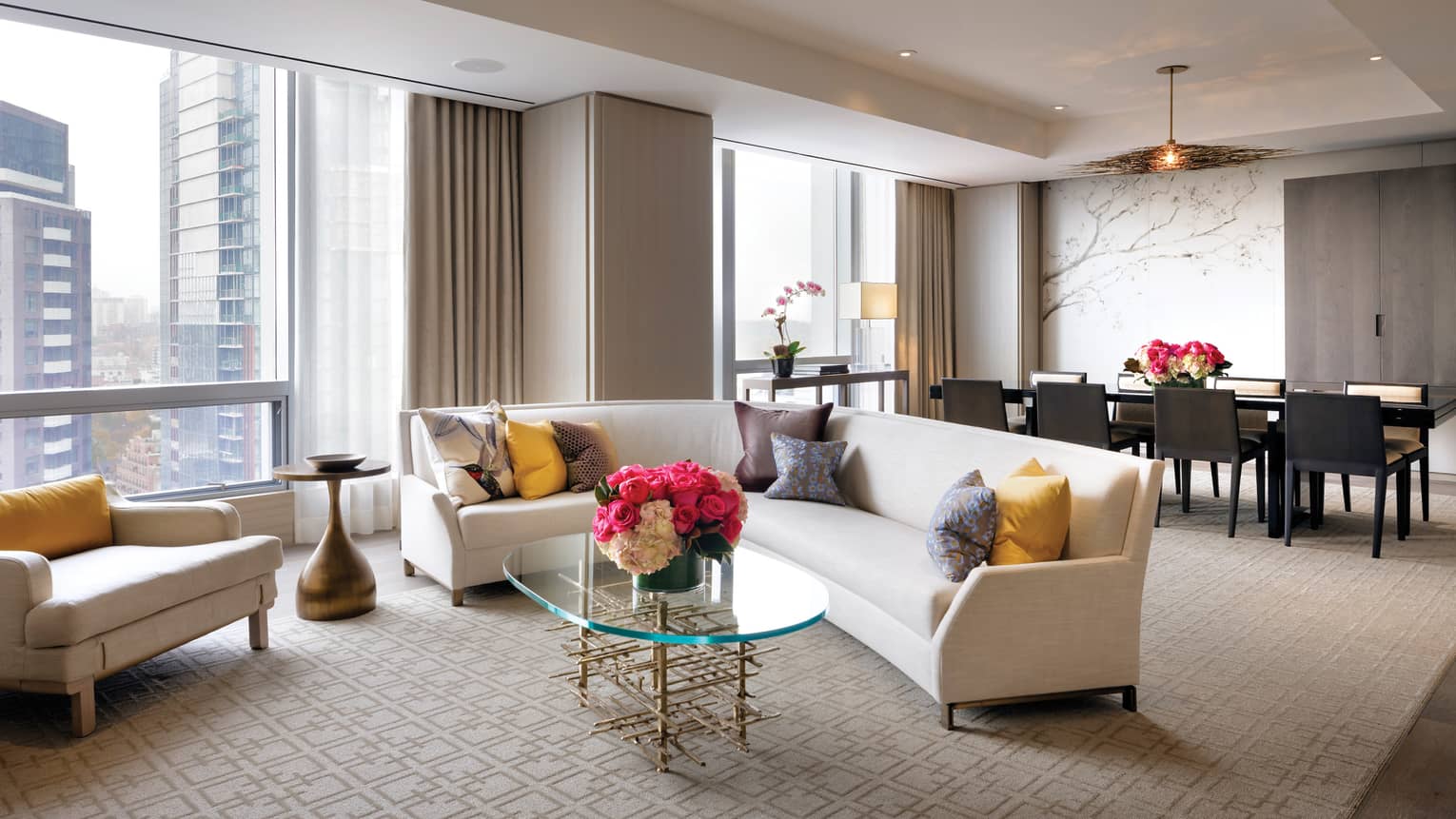Bellair Suite curved L-shaped sofa, colourful pillows, chair under tall sunny windows, by long dining table