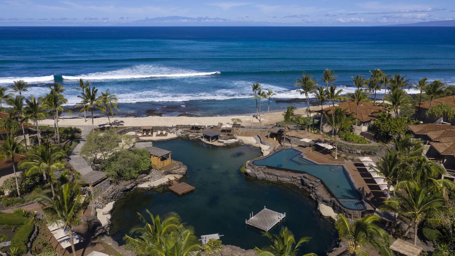 Aerial view of resort pool that mimics a curved pond, palm trees, beach and ocean
