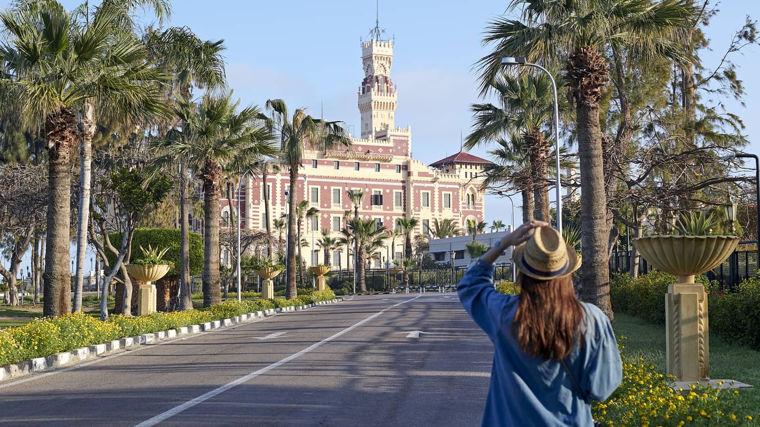 Rear view of a guest approaching a palatial structure with a tall, square tower stretching towards the clear, blue sky.