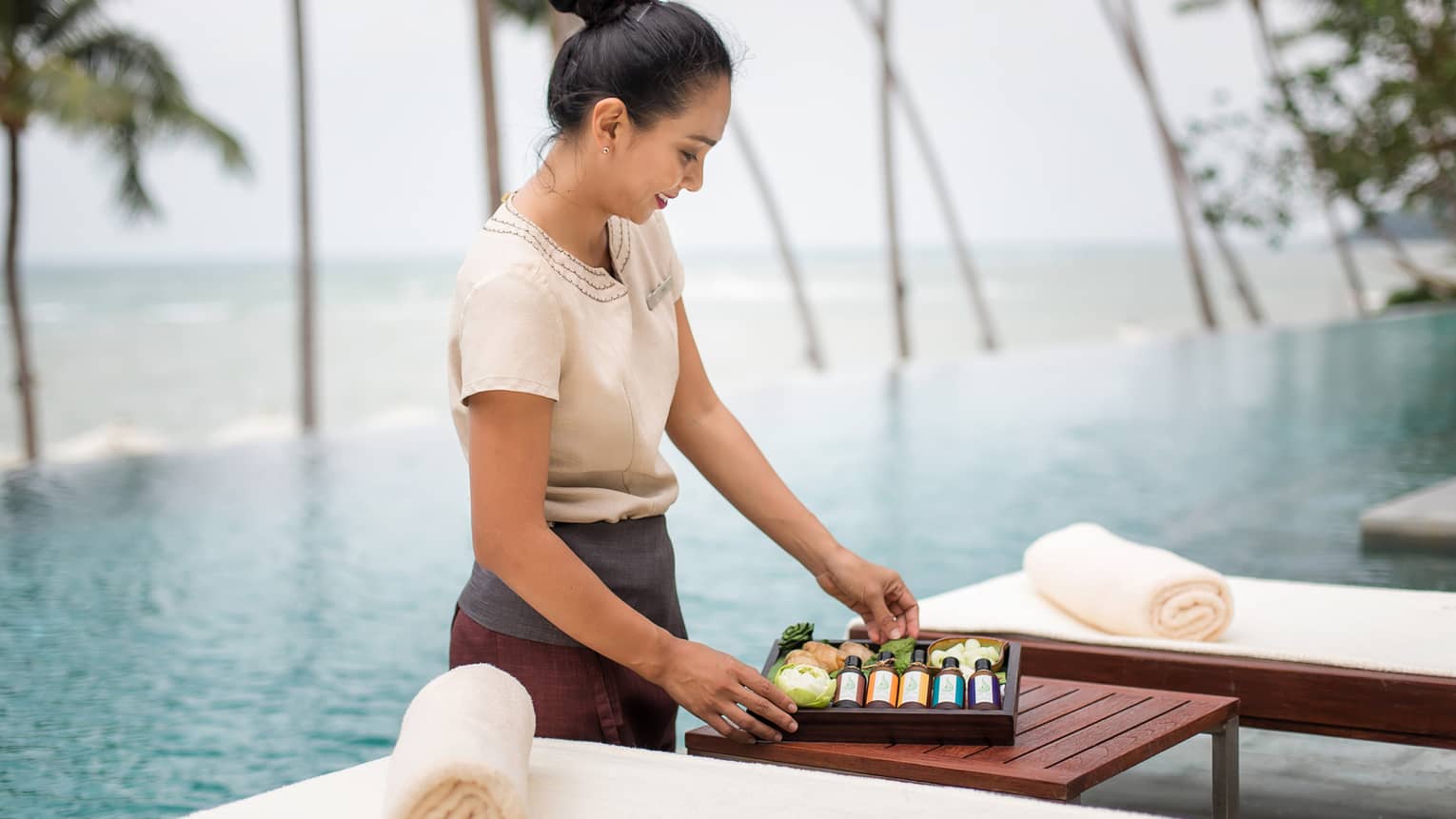 Spa attendant stands in front of swimming pool, holds wood box with bottles, soaps