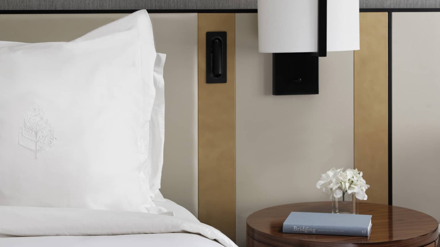 Bed with white linens, round side table with book, reading lamp