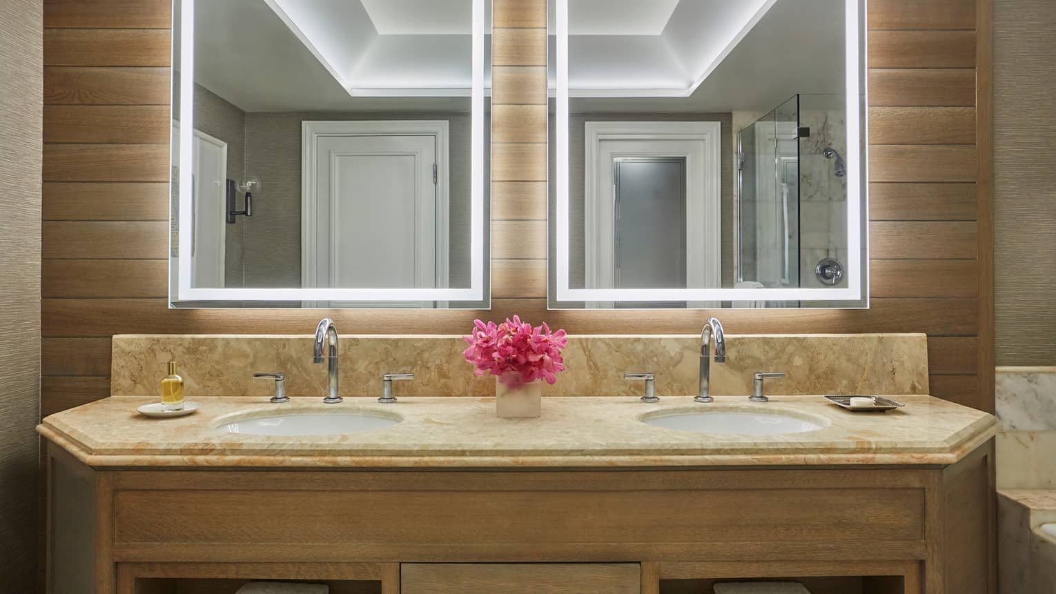 Double bathroom vanity with marble countertop, backlit mirrors and pink flowers in center