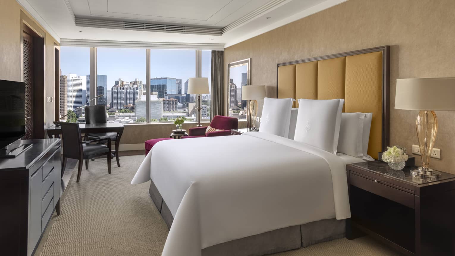 Hotel room with king bed, tan headboard, desk with two chairs, dresser and window-side chaise