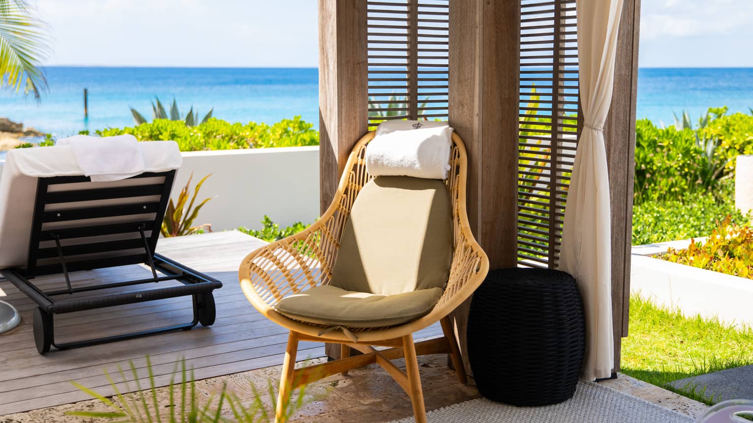 Inside view of a cabana with gazebo walls, flowing curtains and a cane chair; outside a lounge chair overlooks the ocean. 