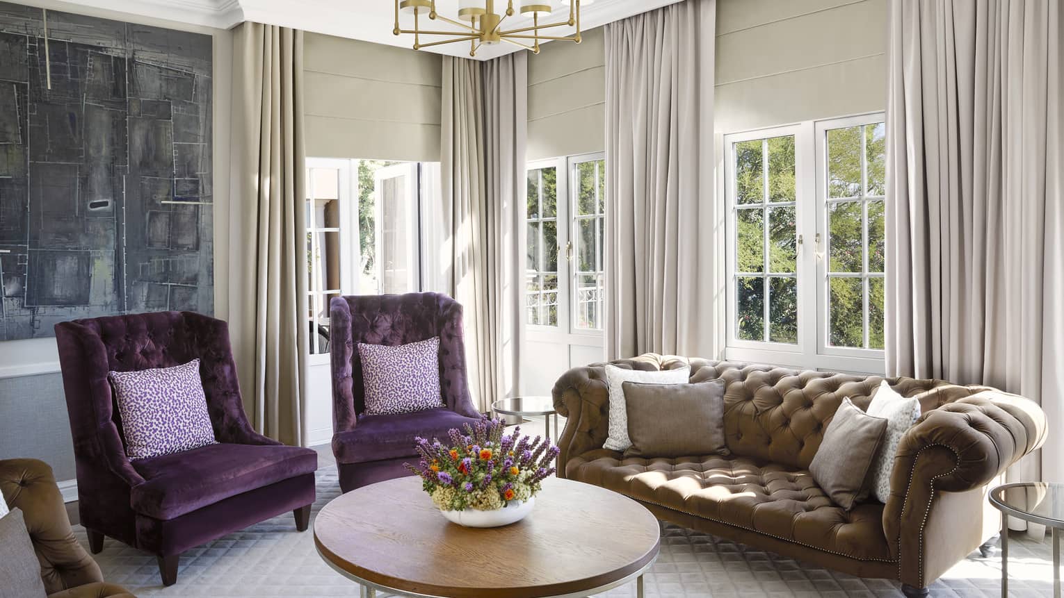 Luxury hotel suite living room with two violet velvet chairs and brown tufted sofa at Four Seasons Hotel Johannesburg