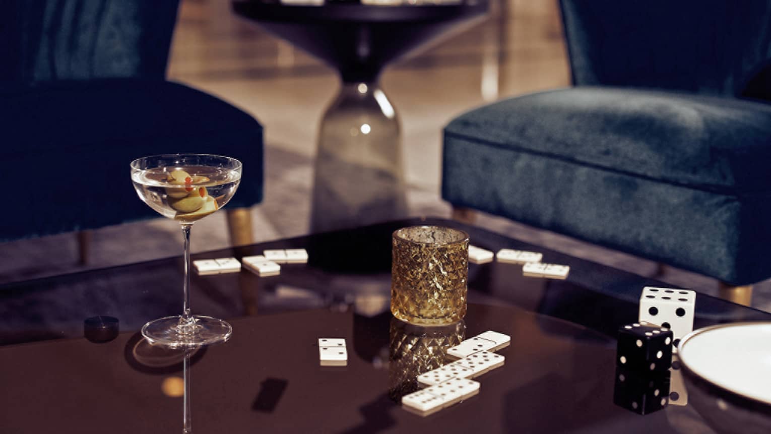 A cocktail next to dominos on a brown table.