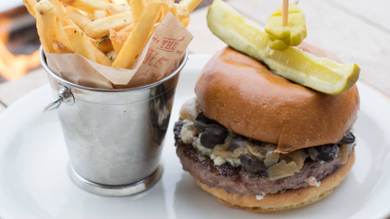 The Handle Burger thick patty on a bun with pickle and pepper spear, fries in silver basket