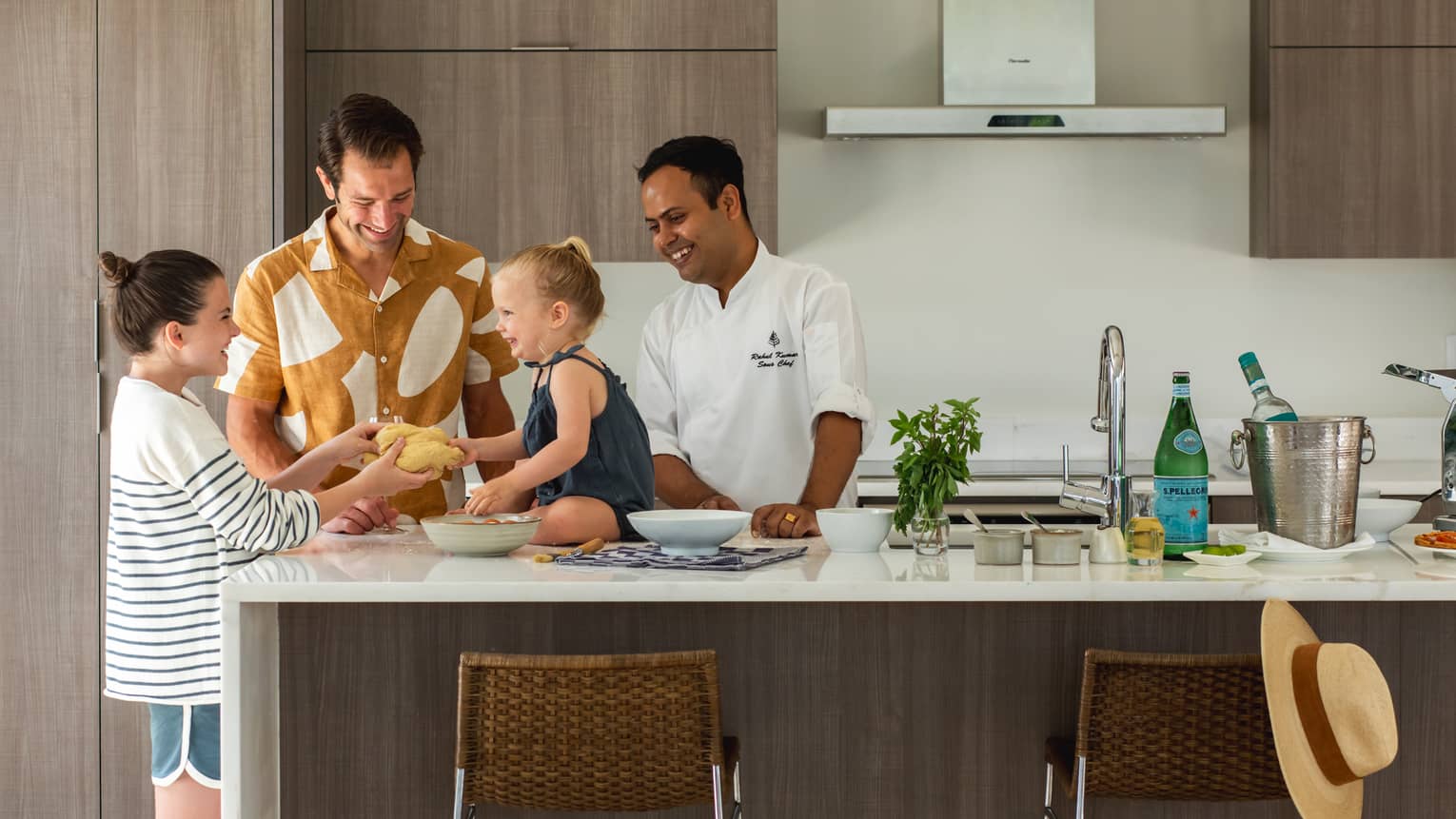 A chef, a father and two children stand in a kitchen smiling as they prepare food together