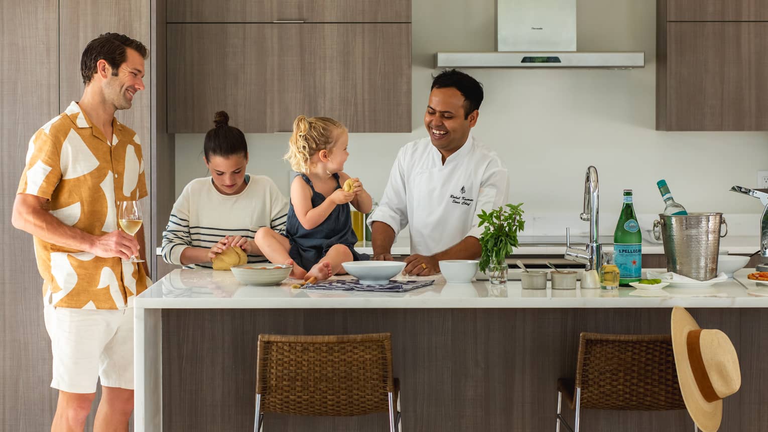 Chefs stands at a kitchen island showing a father and two young children how to prepare a meal