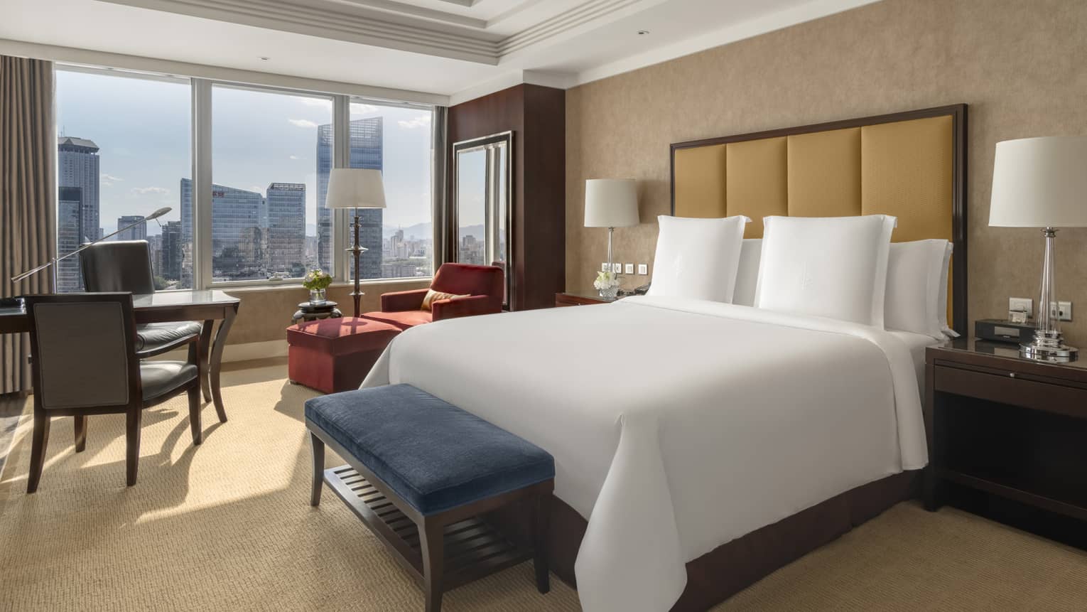 Hotel room with king bed, leather headboard, blue cushioned bench, table with two chairs and windowside chaise