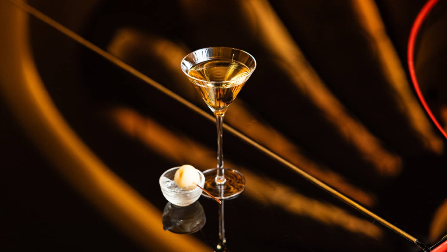 A martini glass on a polished surface holds a pale golden drink.