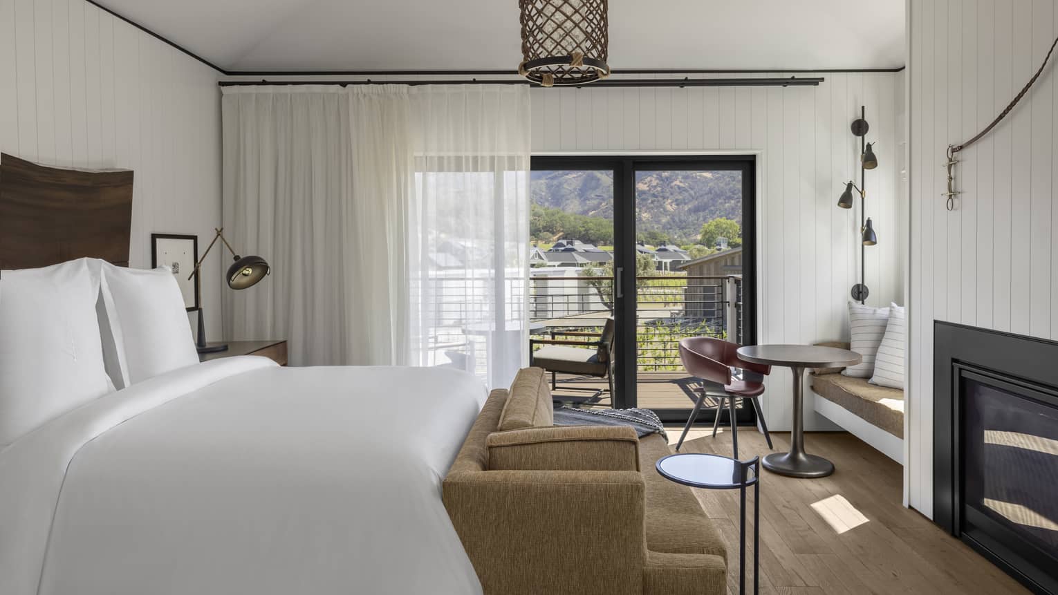 Bright resort bedroom with a king bed, sofa, fireplace, small dining area with built-in seating and sliding glass doors opening to a balcony with mountain views