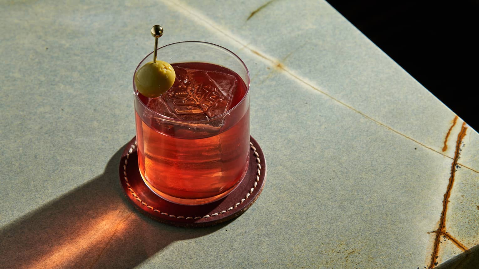 Red-coloured cocktail in a rocks glass garnished with a green olive