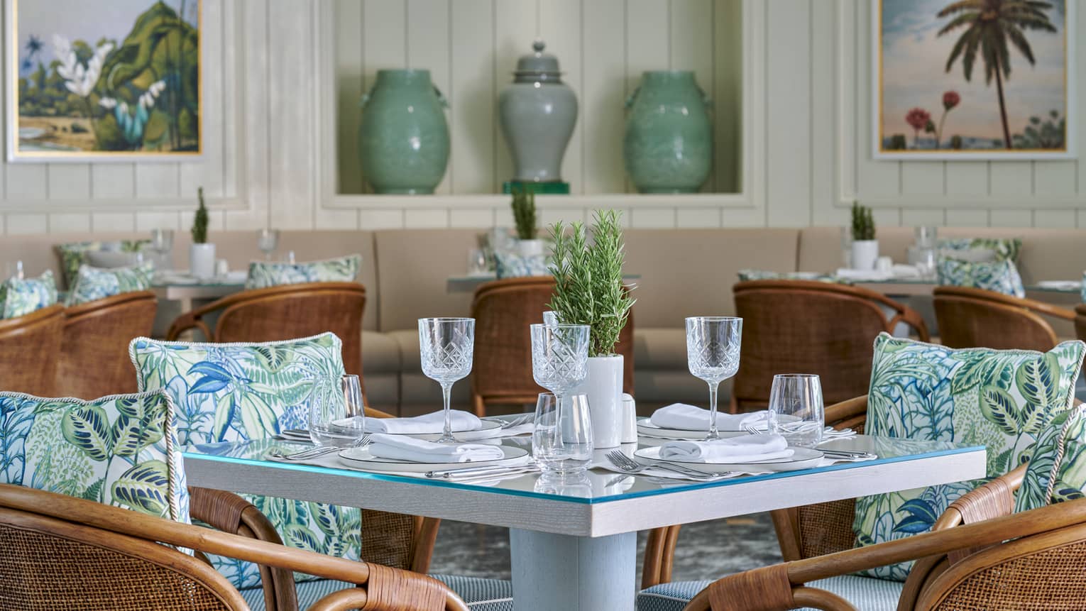 Byblos indoor dining area with rattan chairs and blue patterned accent pillows, square glass-topped tables