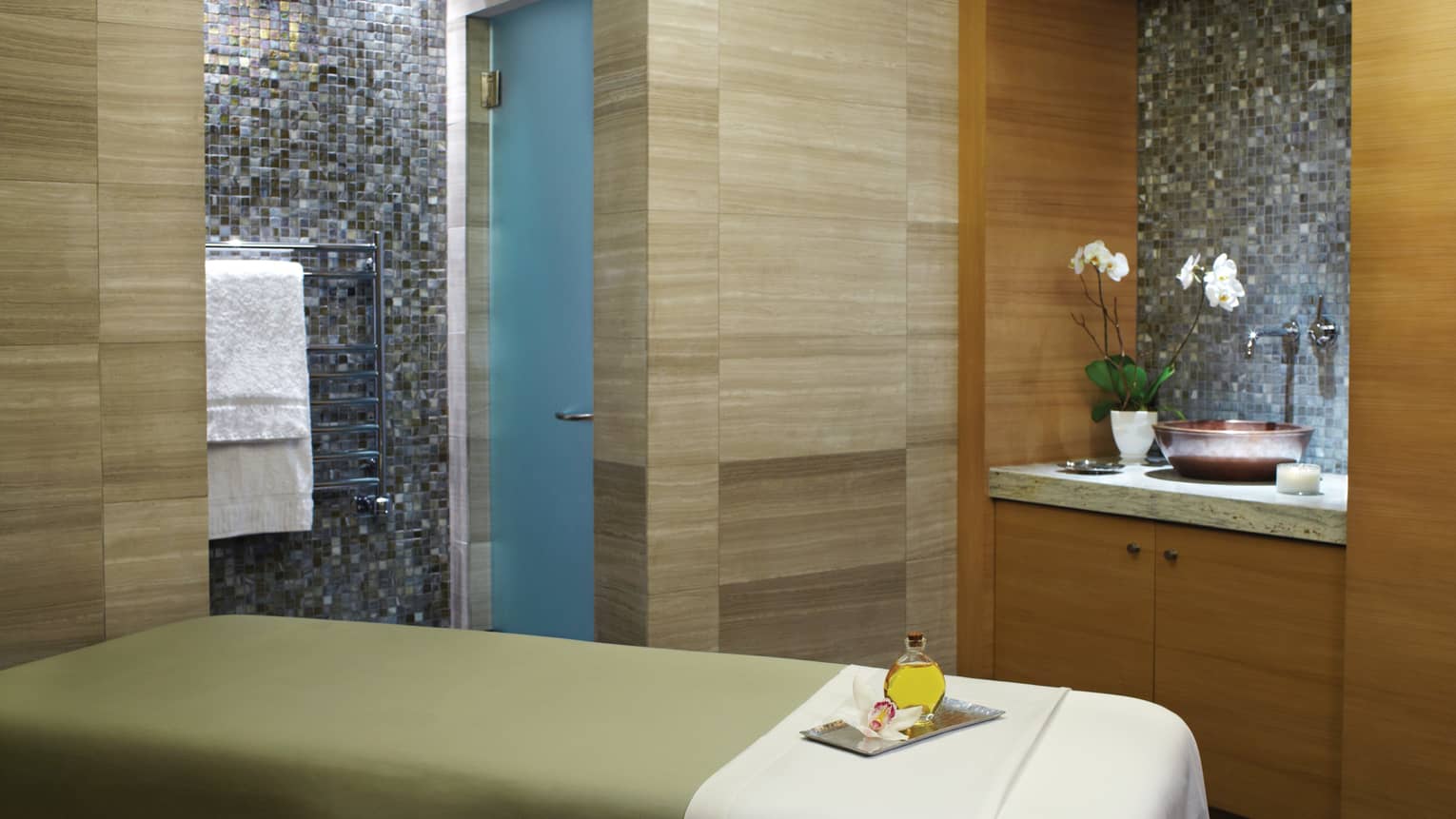 Massage table with green blanket, white sheet, wood and tile walls, sink