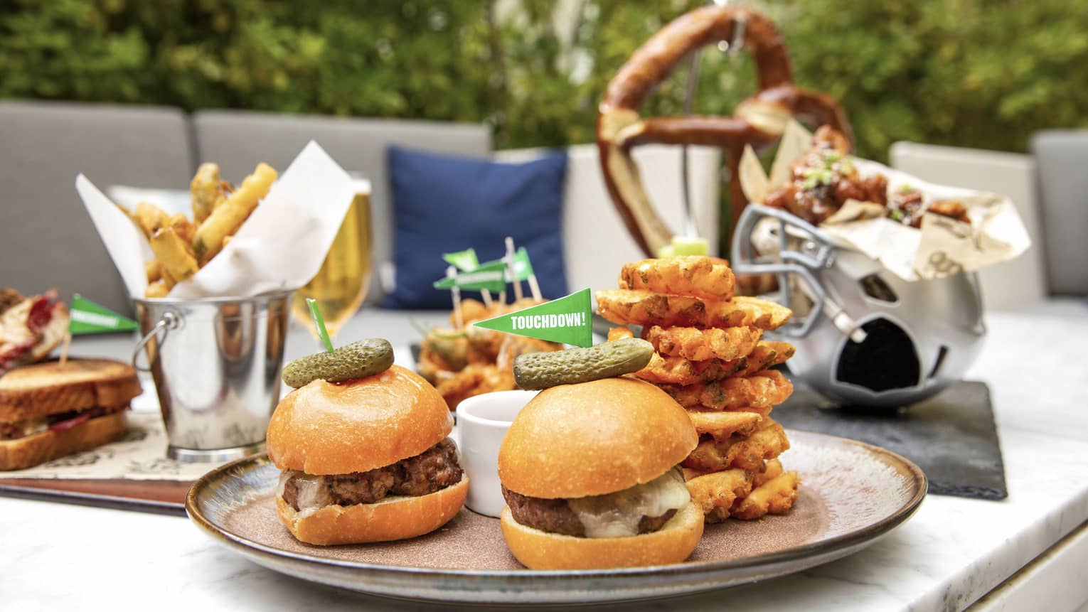 A plate of burgers and fries next to chicken wings and sandwiches, all outside.