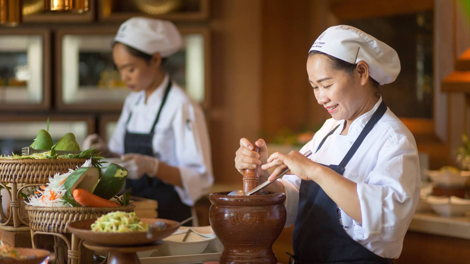 Two chefs in uniform prepare authentic Thai cuisine dishes at counter with fresh vegetables