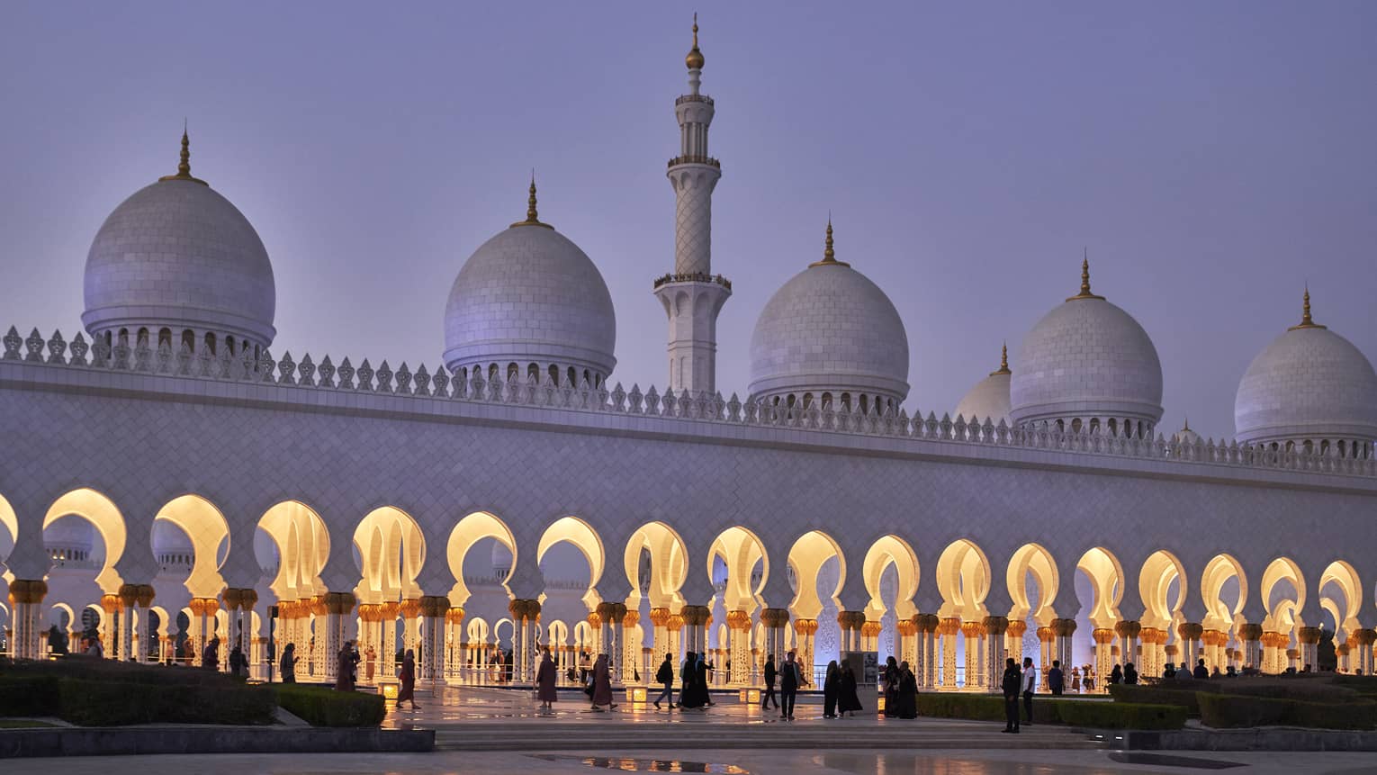 Stunning white marble mosque at dusk features a minaret with pointed domes at either side; keyhole arches line the entrance.