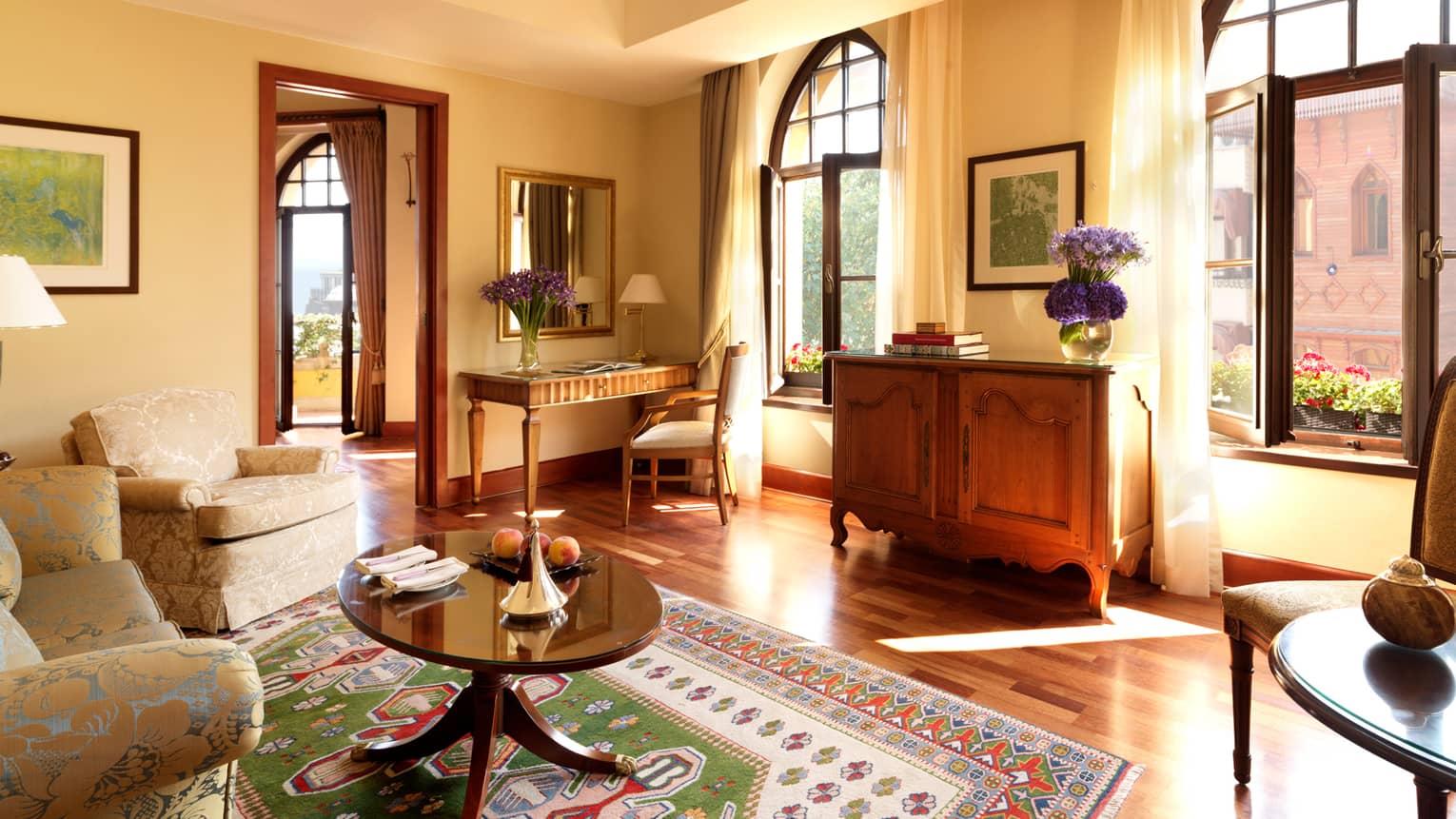 Deluxe Suite bright living room with table over colourful kilim carpet, large windows