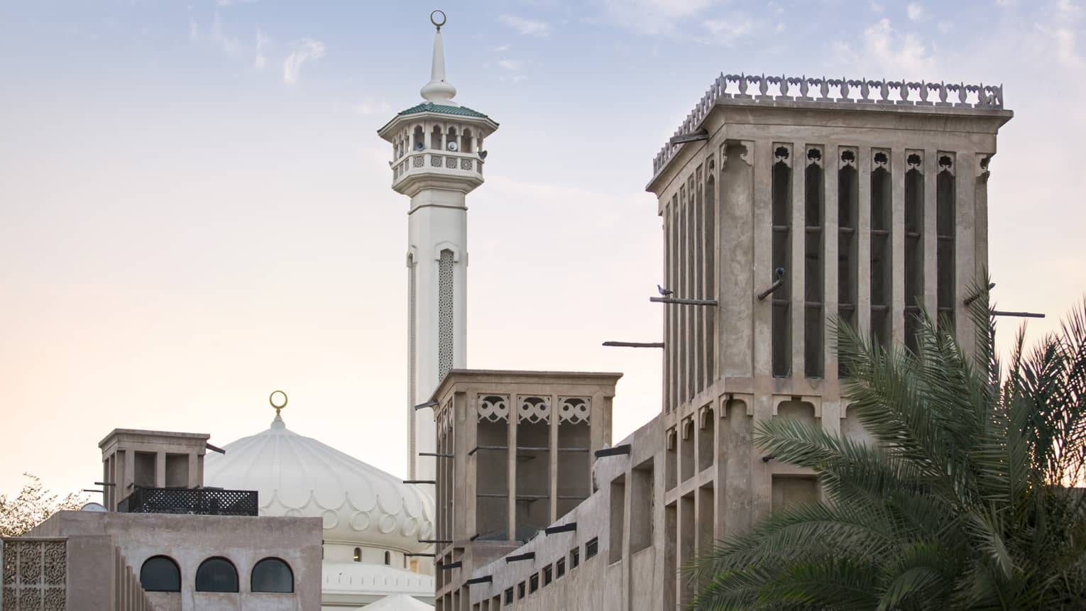 Street view of a mosque with a domed roof and adjoining minaret; in the fore, adobe buildings featuring ornate wind towers.