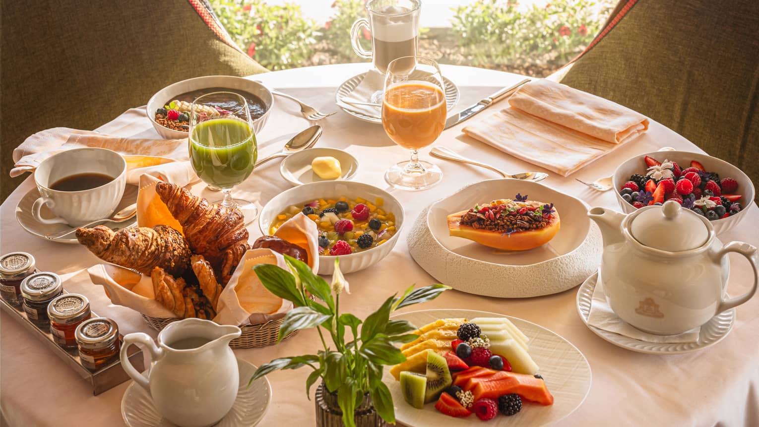 A round table in front of a window, set with an array of brunch dishes and beverages