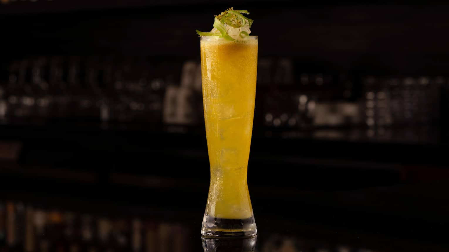 A tall glass with a yellow cocktail inside.