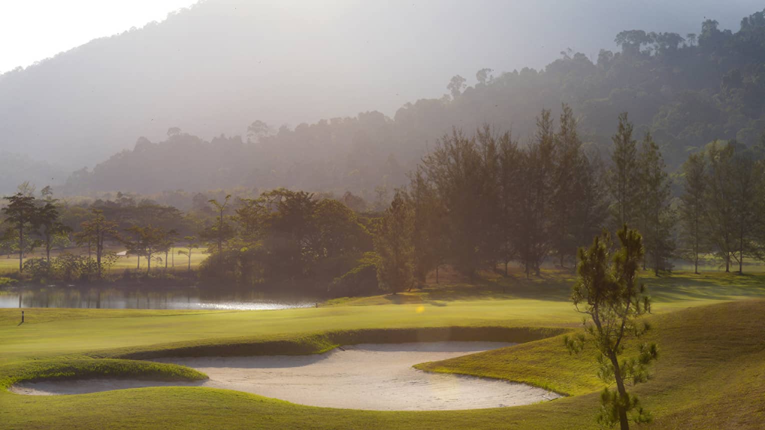 Misty golf course green, sand trap, mountains in background