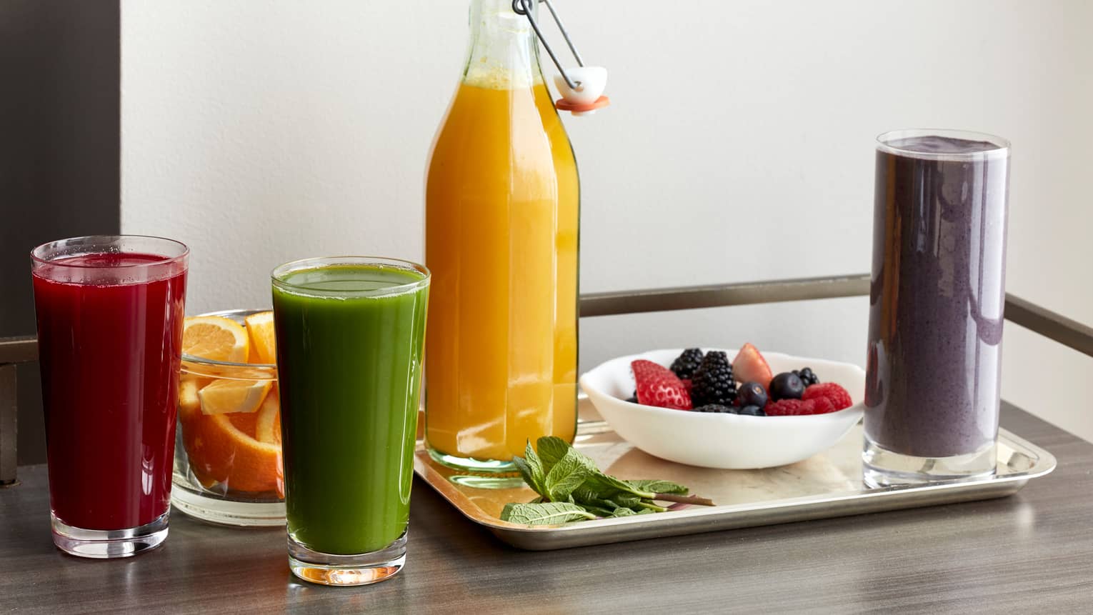 A table filled with various smoothies, a fruit bowl, and a bottle of orange juice