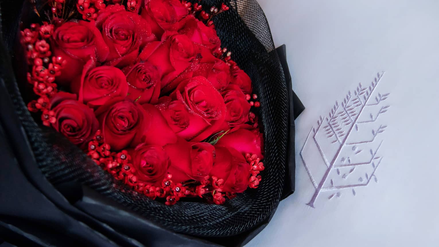 Bouquet of red roses wrapped in black fabric laying on a white pillow with the Four Seasons logo