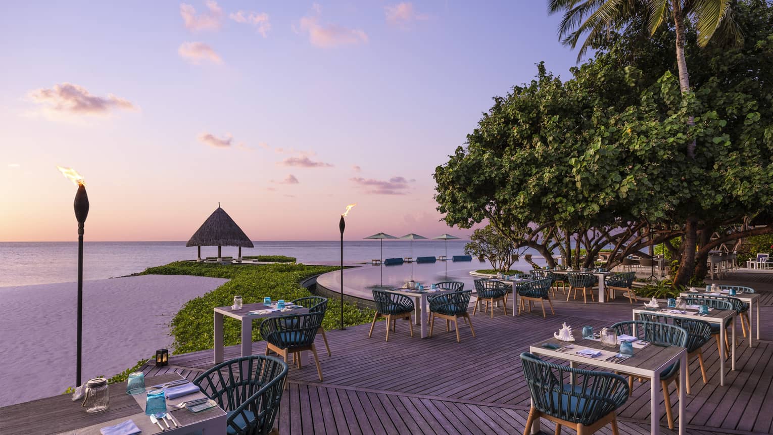 Tiki torches line the oceanside Reef Club terrace that's ready for guests with tables set with plates, silverware, blue napkins, all overlooking the ocean
