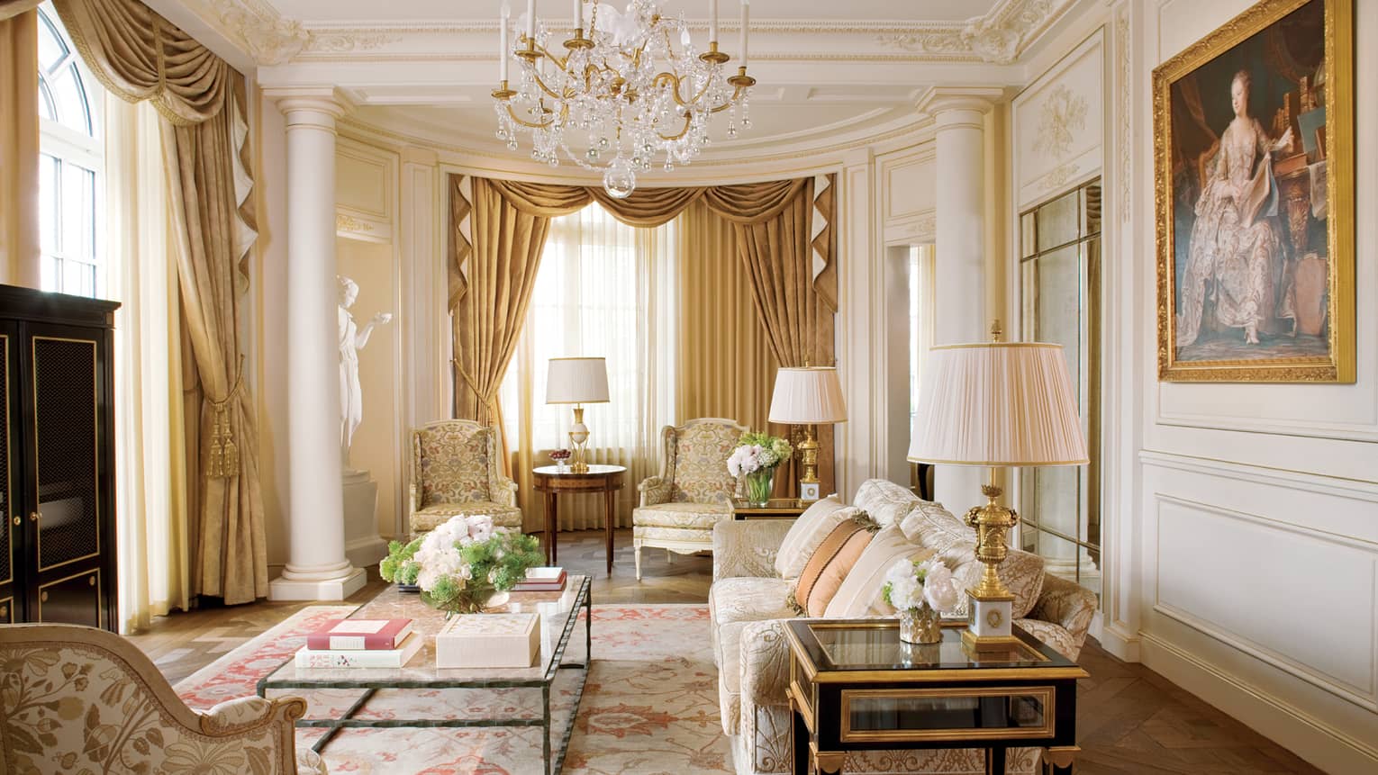 Elegant Royal Suite living room with cream floral sofas and decor, crystal chandelier, white statue, large oil painting