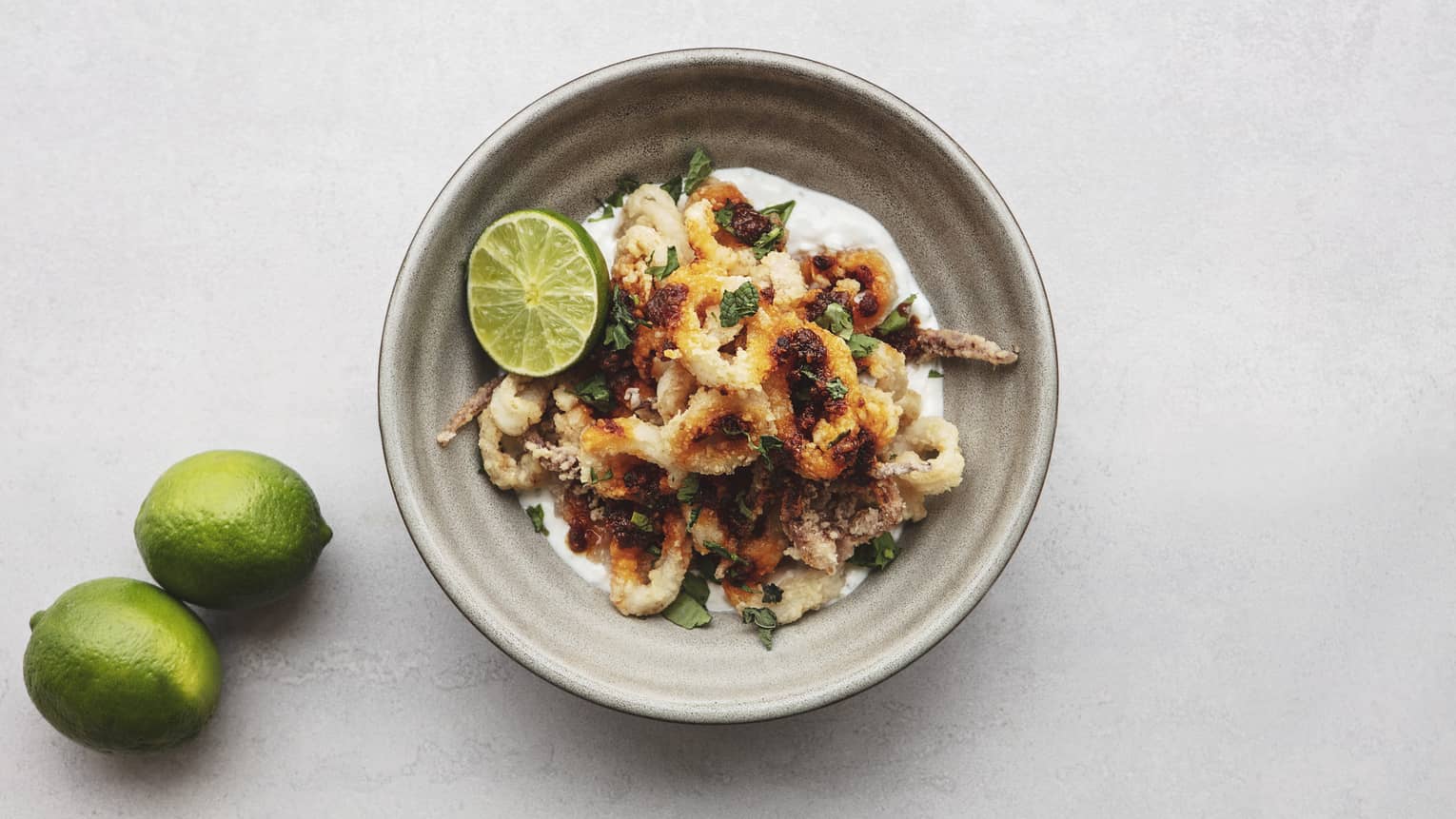 Bowl of crispy fried calamari, topped with chopped herbs and lime