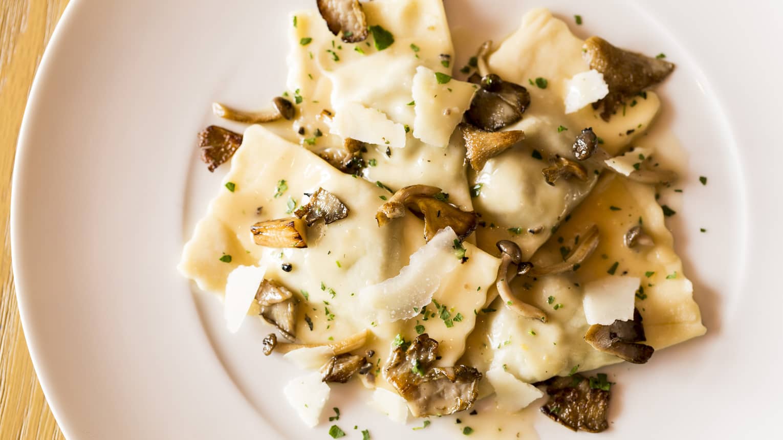 Veal Ravioli pasta garnished with shaved parmesan cheese, mushrooms on plate