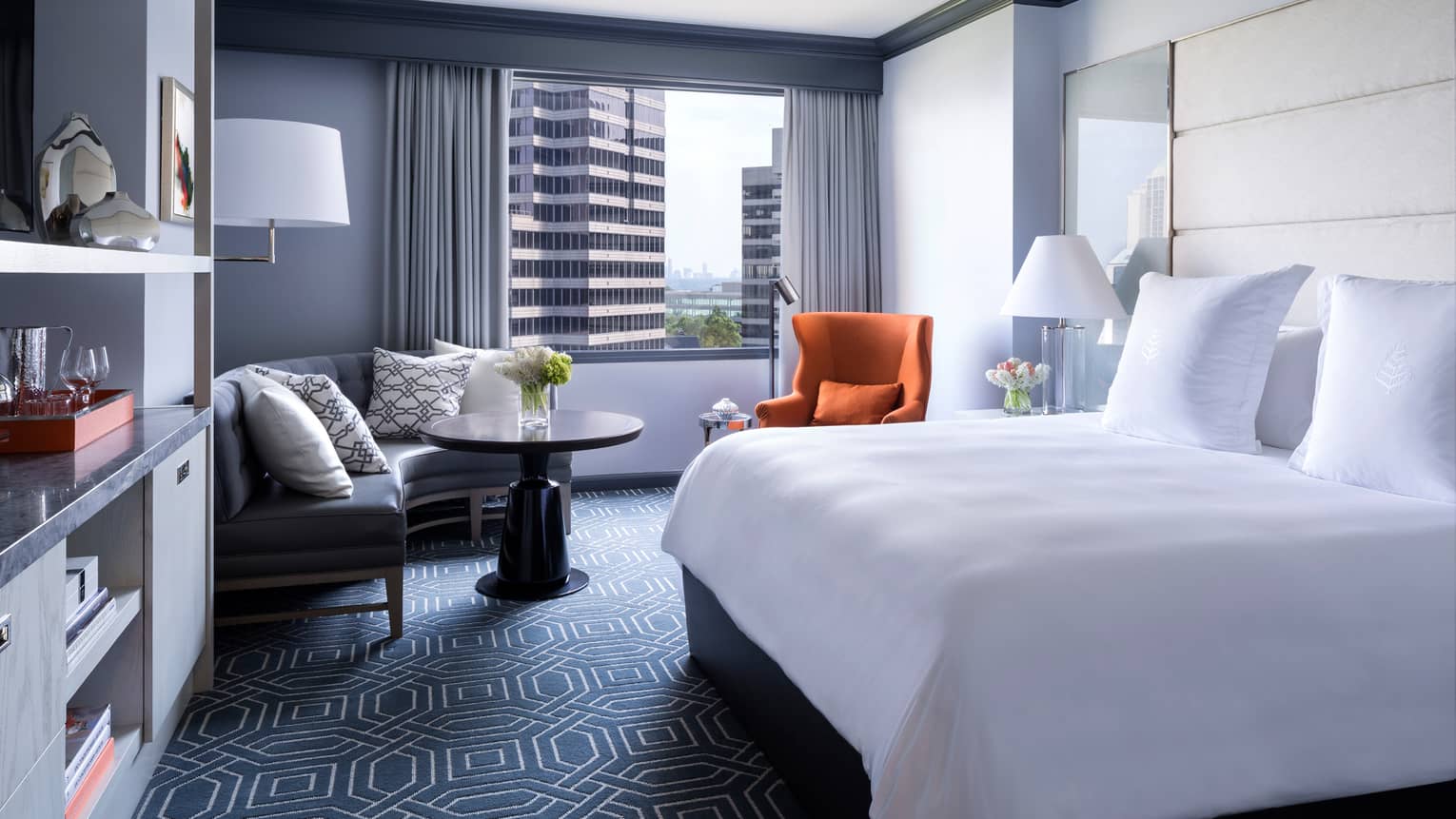 Midtown Deluxe Room bed, blue carpet, marble bar, curved corner sofa, orange accent chair