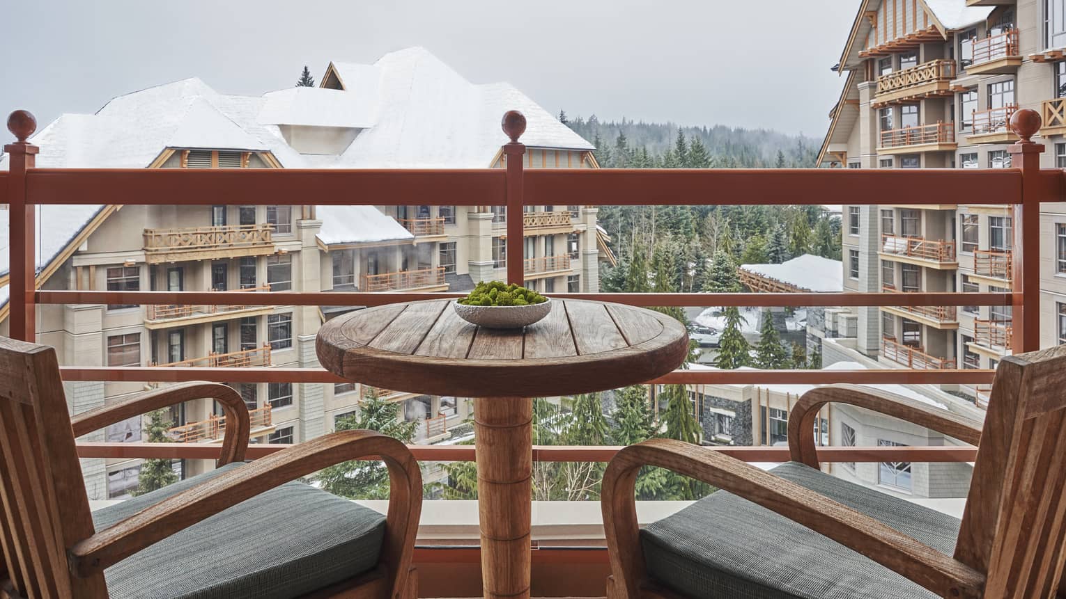 Two wooden arm chairs and a small table on a balcony overlooking Four Seasons Resort Whistler