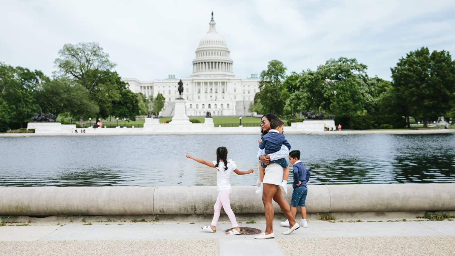 Woman and three children walk in front of the Capitol reflecting pool in Washington, DC, with Capitol building in background