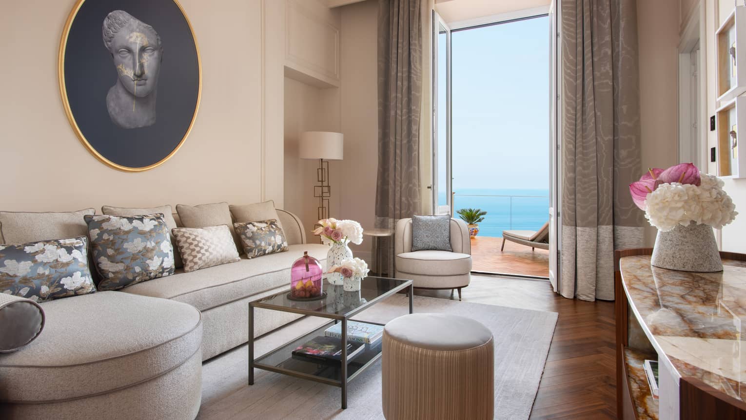 Living room with curved, taupe-coloured sofa, doors leading to ocean-view balcony