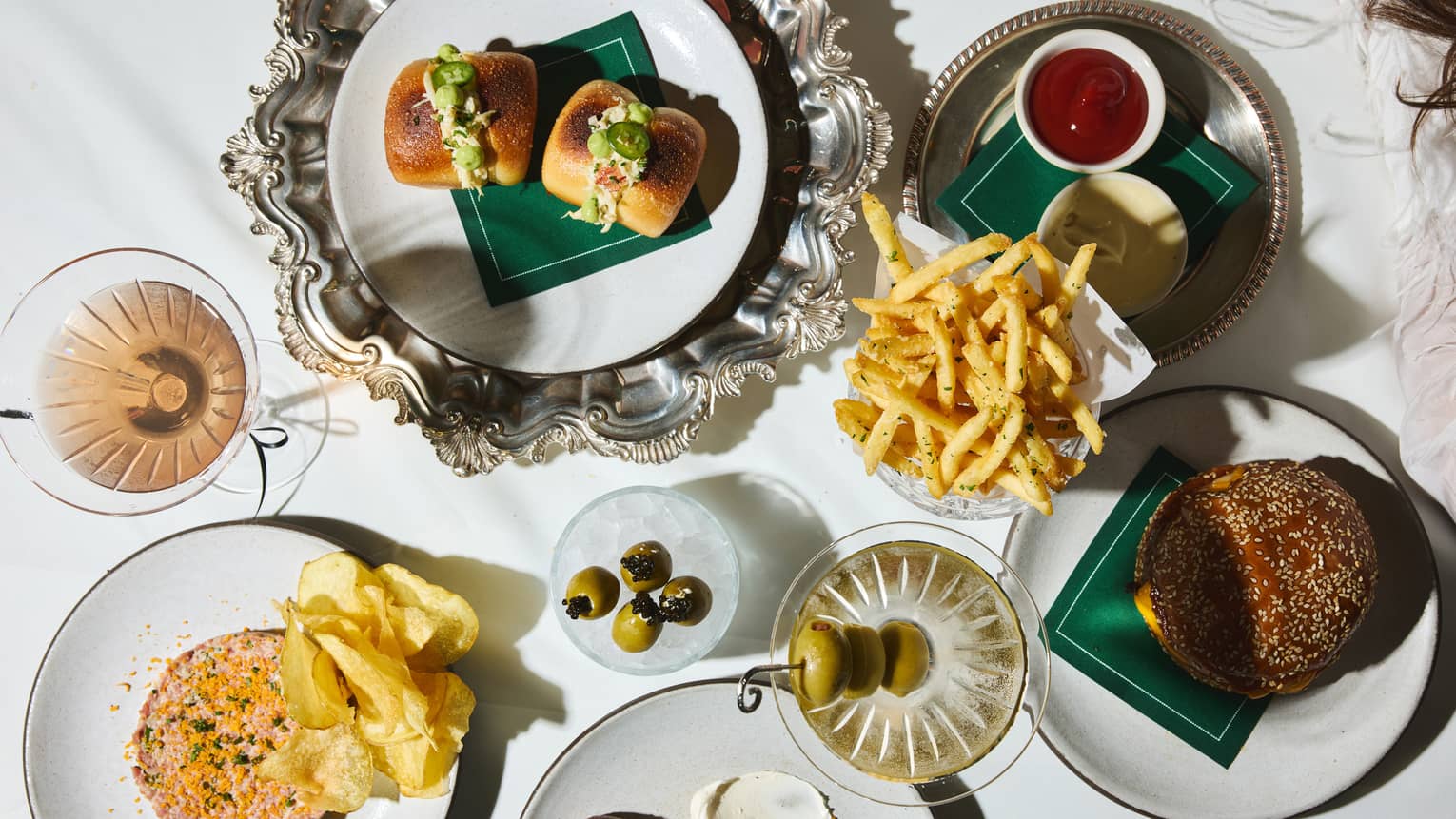 Overhead view of dining table filled with small white plates of food, decorative silver platters and cocktails