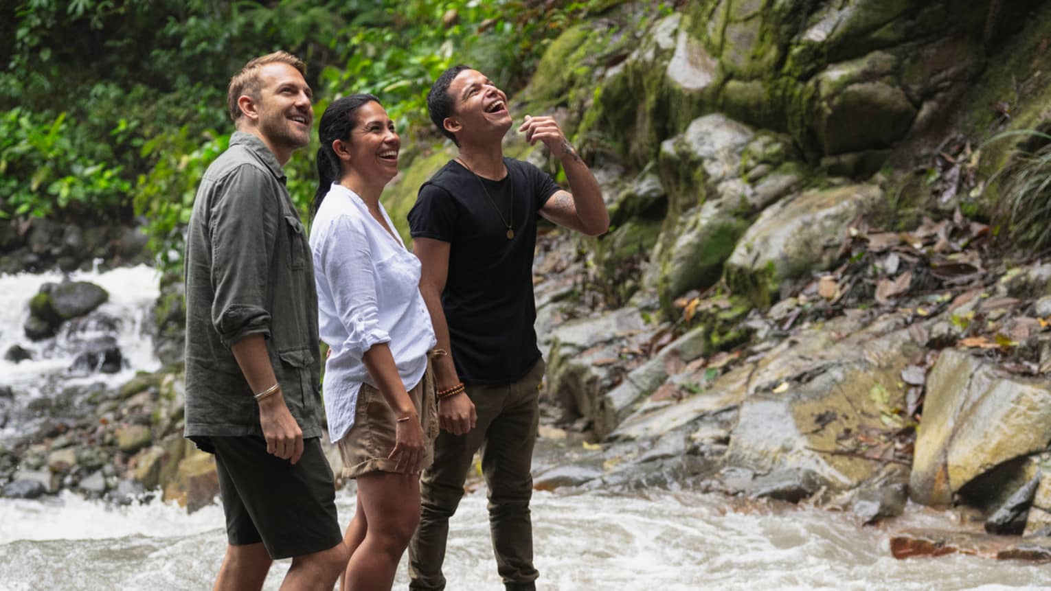 ,Three people stand together on some rocks in the middle of a river as they all look up at the sky