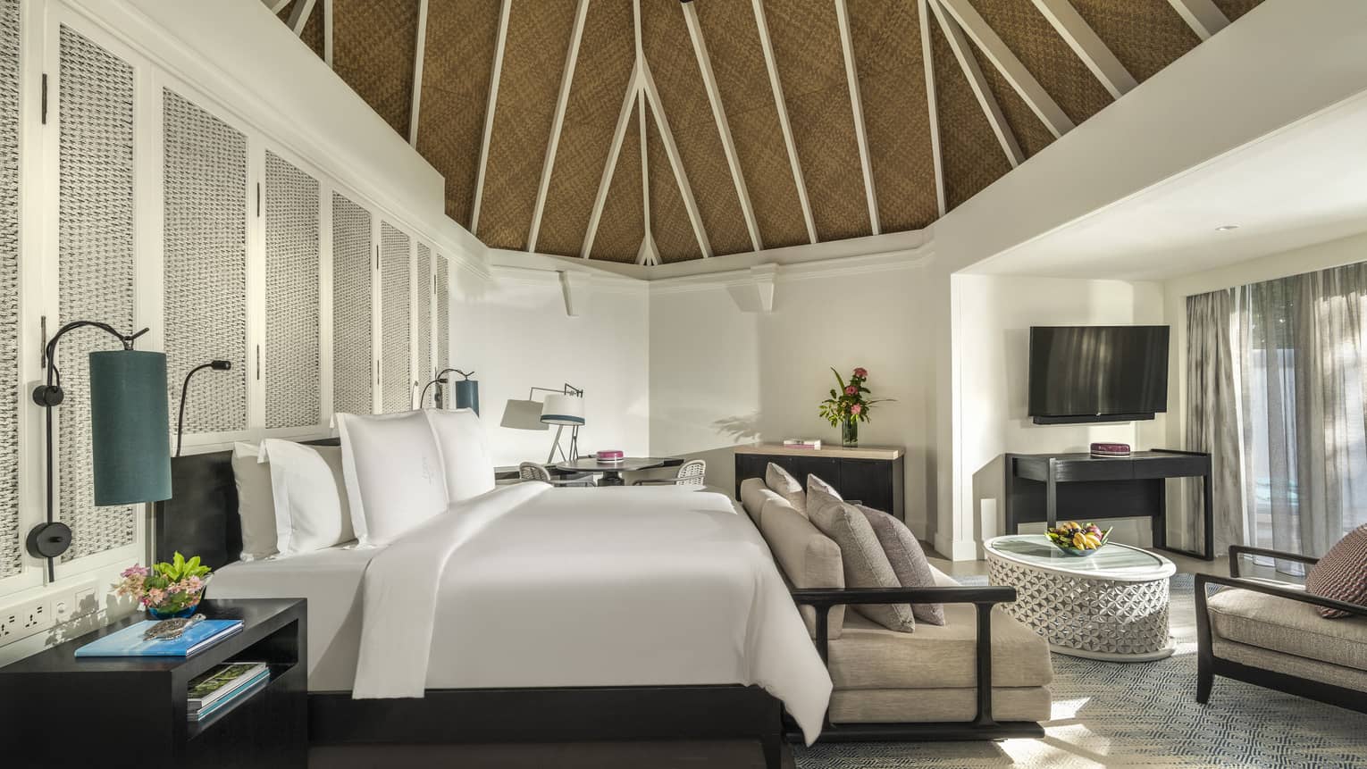Beach pavilion bedroom with a king-size bed, vaulted thatched ceiling, cozy seating area and a flatscreen TV