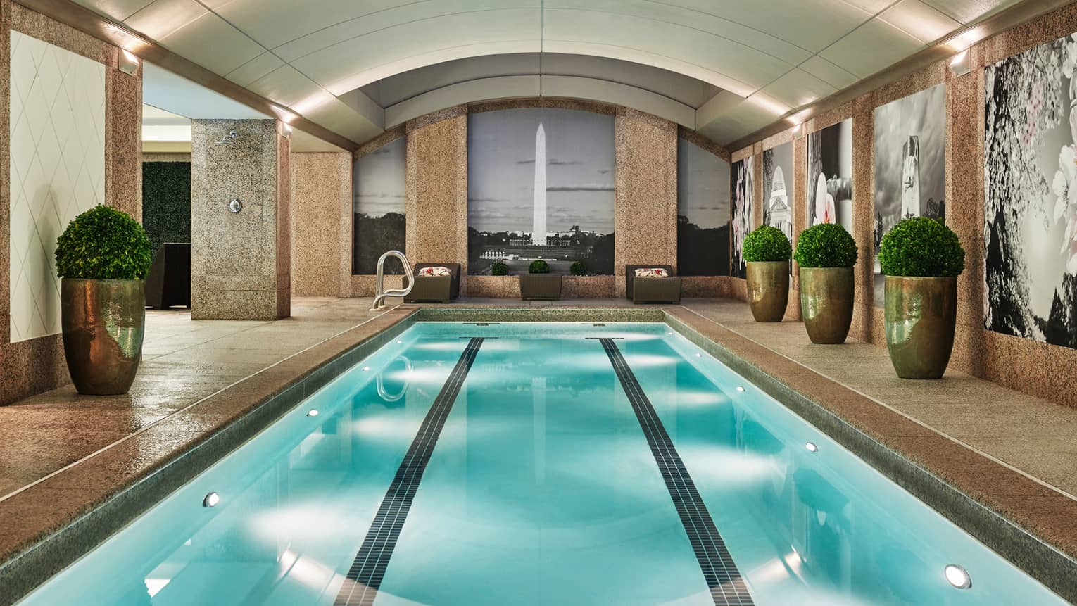 Long indoor lap swimming pool, large gold planters on deck, wall with black-and-white mural of the Washington Monument